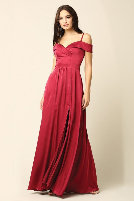 Femme portant une robe de soirée longue en satin bleu marine, coupe épaules dénudées avec fente haute sur la jambe, tenant une pochette dorée.