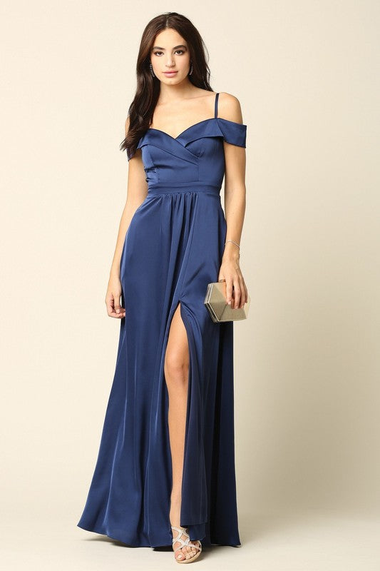 Femme portant une robe de soirée longue en satin bleu marine, coupe épaules dénudées avec fente haute sur la jambe, tenant une pochette dorée.