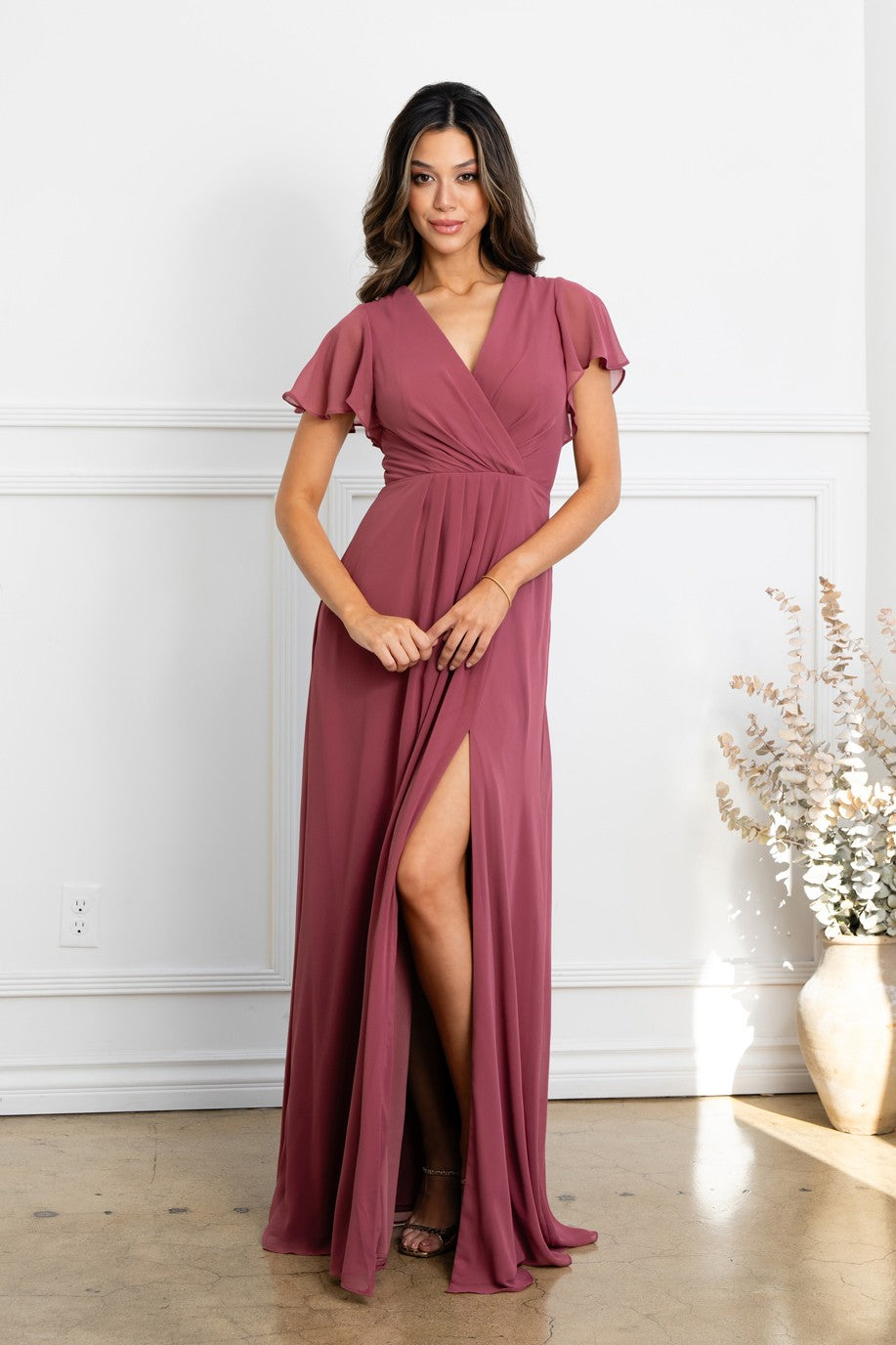 Robe longue de soirée desert rose avec décolleté en V croisé, manches courtes évasées et fente haute sur la jambe.