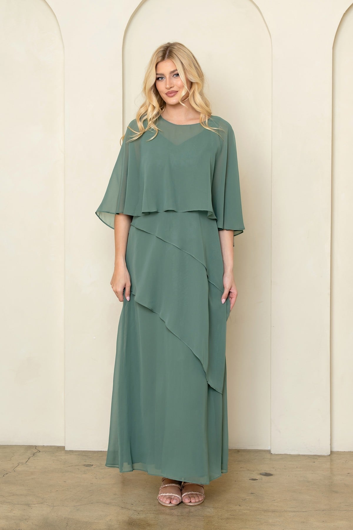 Robe de soirée longue eucalyptus en mousseline fluide avec superposition style cape sur les épaules et jupe à volants asymétriques. Coupe élégante et classique pour occasions formelles.