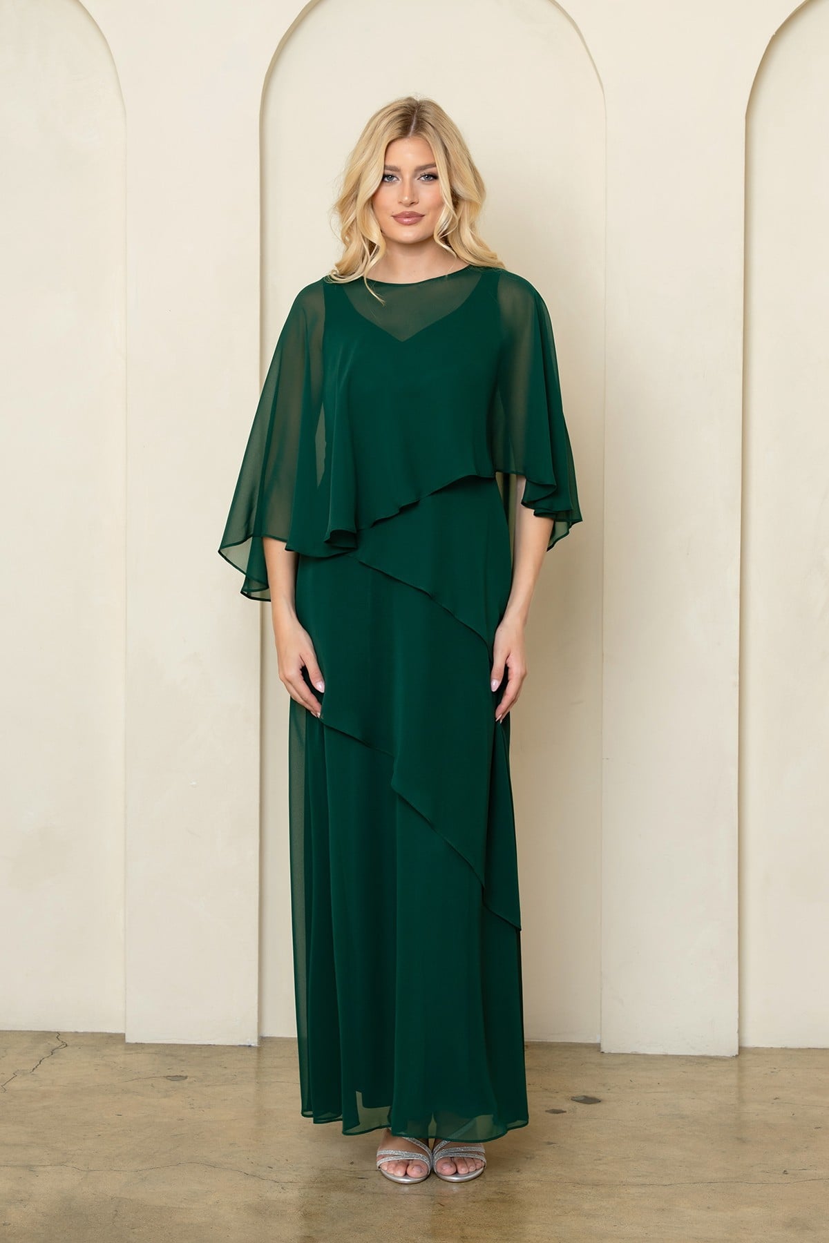 Robe de soirée longue vert en mousseline fluide avec superposition style cape sur les épaules et jupe à volants asymétriques. Coupe élégante et classique pour occasions formelles.