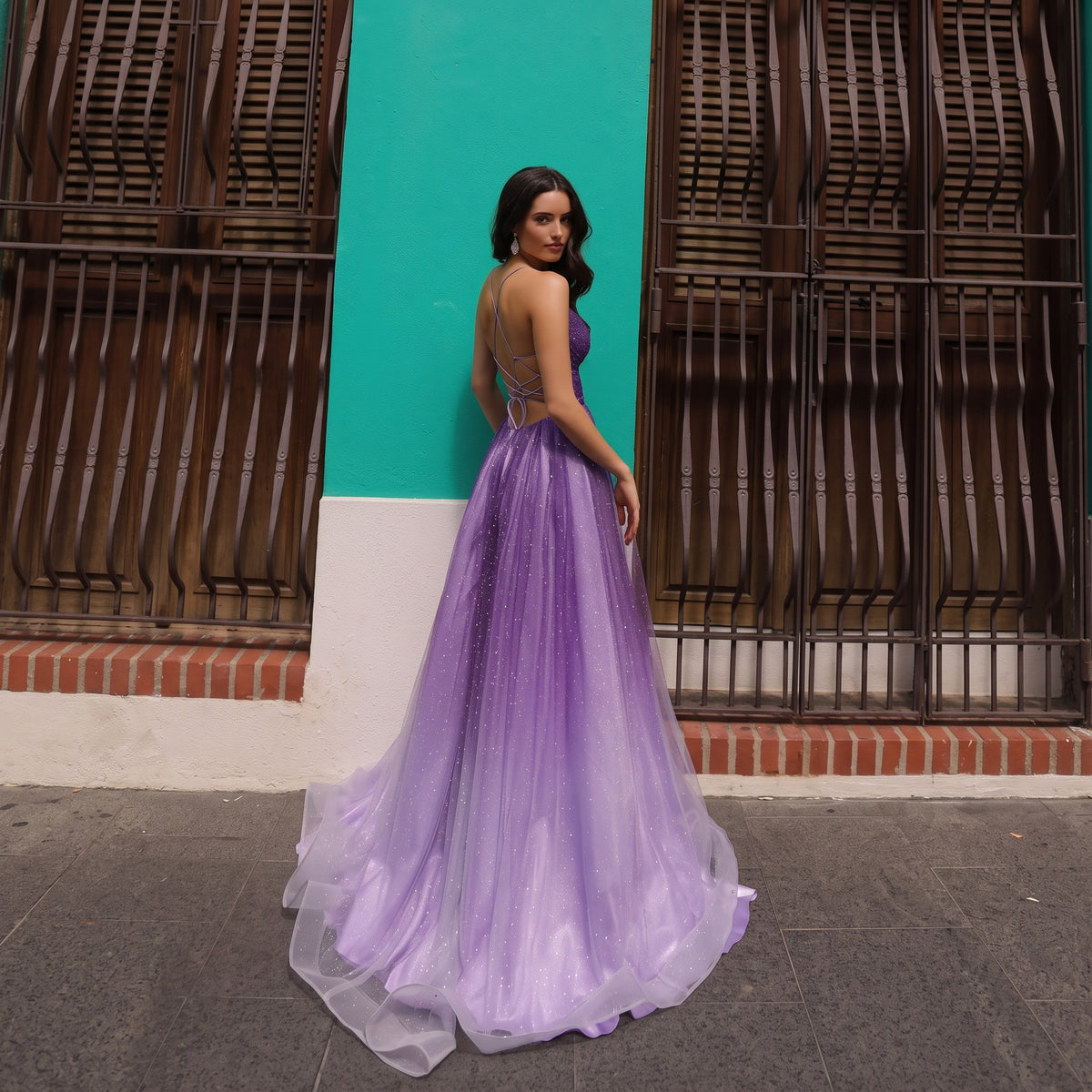 Vue arrière d'une robe de soirée longue montrant le dos nu à laçage croisé et la traîne fluide en tulle scintillant dégradé.