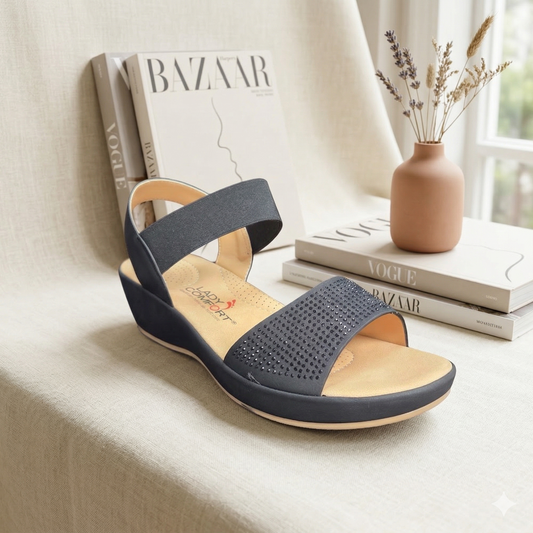 Sandale compensée noire modèle Felicity de Lady Comfort. Bride avant ornée de micro-cristaux noirs et semelle intérieure ergonomique coussinée, présentée devant des magazines de mode Vogue et Bazaar.