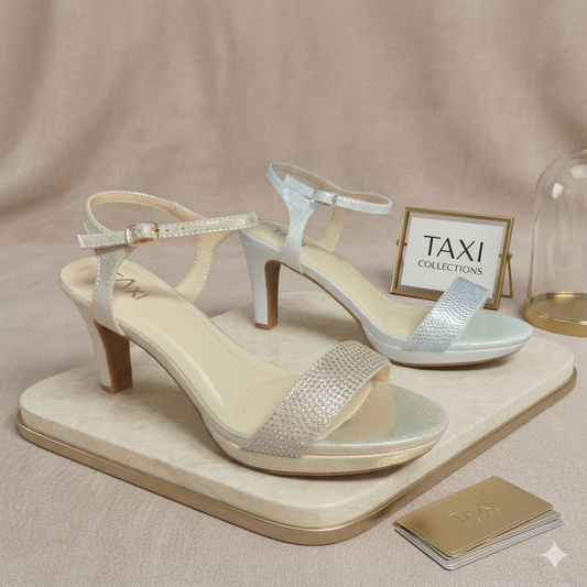 Paire de sandales Linda de Taxi Collections en champagne et argent. Modèle à talon haut, plateforme avant et bride à strass scintillants sur un plateau de marbre.